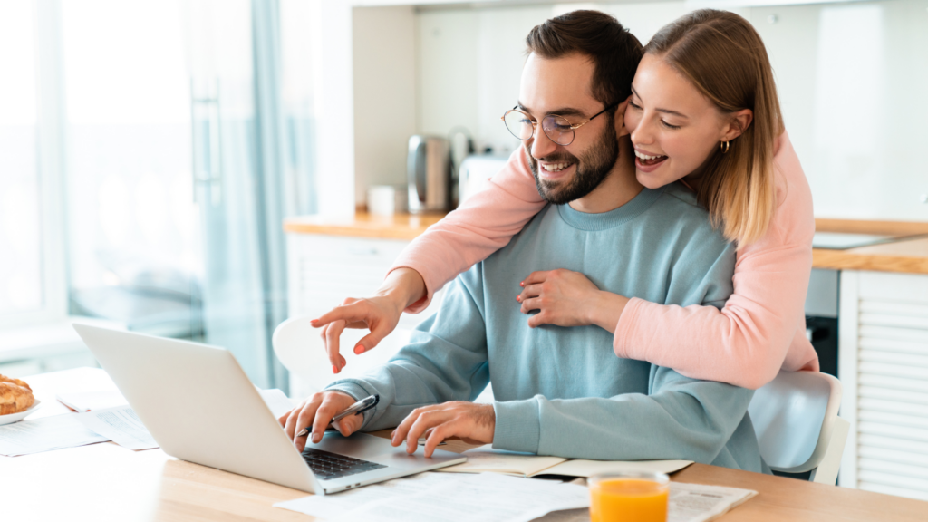 Investment Property vs. Owner-Occupied Properties - Image of happy couple looking at something on a laptop at the home work desk