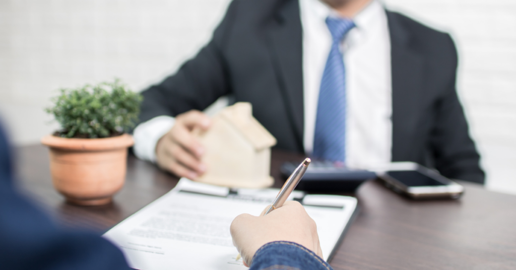 SMSF Property - Image of a person signing a loan agreement and a broker is sitting with a dummy home infront of him